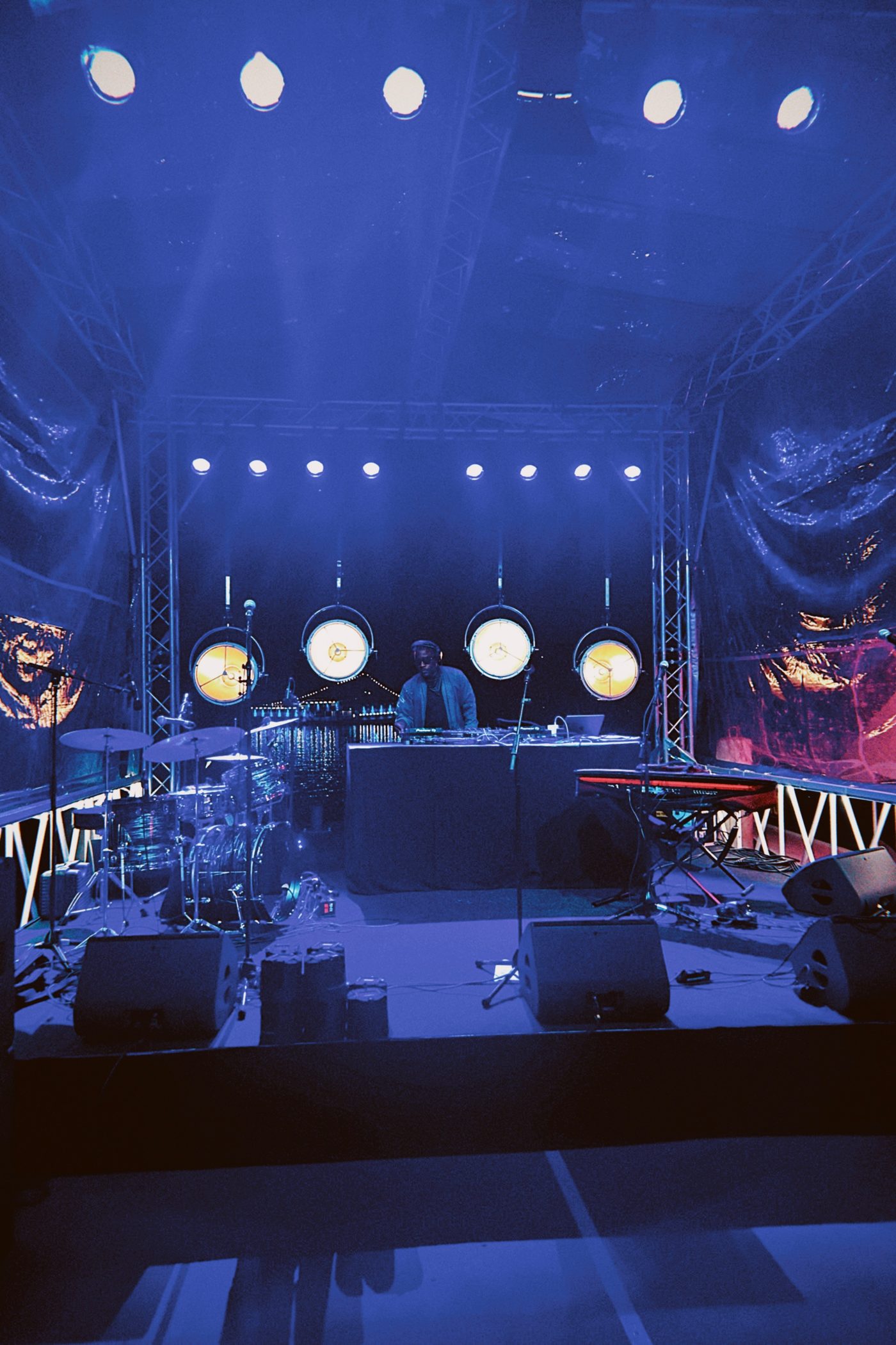 A full stage in blue light, Chris at the decks between the drums and keys